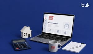 Laptop con el Portal Empresarial Infonavit, una pequeña casa, calculadora y taza de café sobre fondo azul. 