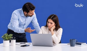Colaborador señalando a una mujer estresada frente a su laptop en la oficina, representando un caso de acoso laboral.