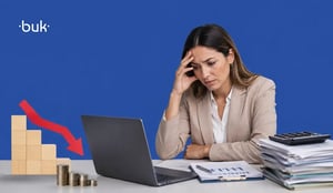 Mujer preocupada frente a laptop con papeles, monedas y gráfico descendente reflejando inestabilidad laboral.