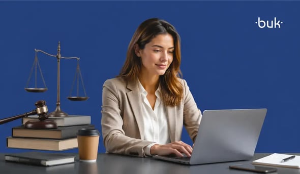mujer trabajando en laptop junto a libros de derecho, mazo y balanza de justicia sobre fondo azul.