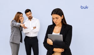 Mujer abrazando su laptop mientras dos personas susurran y la señalan, reflejando incivilidad laboral. 