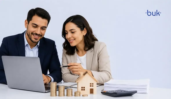 Profesionales sonrientes revisando una laptop junto a casa modelo y monedas sobre cálculo de puntos infonavit. 