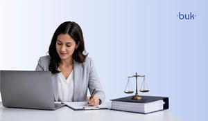 Mujer redactando reglamento de trabajo en su escritorio. Enfrente de ella una laptop y una carpeta y una balanza.