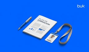 Manual con un plan de formación laboral sobre escritorio azul; a un costado aparece un bolígrafo y del otro la identificación de un colaborador.