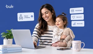 Madre en su escritorio con su bebé frente a una laptop, como ejemplo de la maternidad en el trabajo.