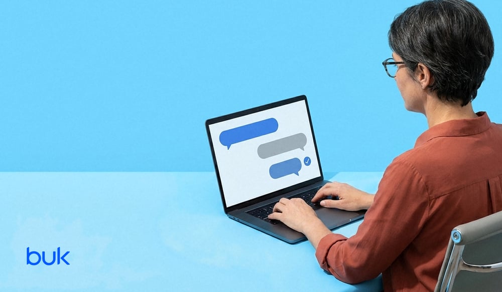 Persona usando un asistente de chat en su laptop, vista por encima del hombro, sobre fondo celeste